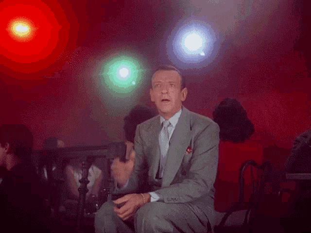 a man in a suit and tie is sitting in a chair in front of a crowd .