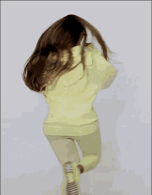 a young girl in a yellow hoodie and green pants is running .
