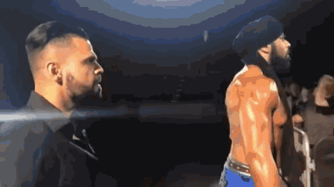 two men are standing next to each other in a dark room in a wrestling ring .