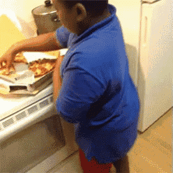 a young boy in a blue shirt reaches for a pizza on a counter