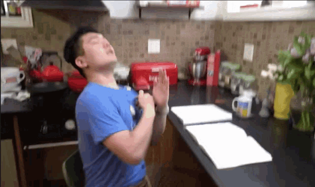 a man in a blue shirt is sitting in a kitchen with a red container that says ' milk ' on it