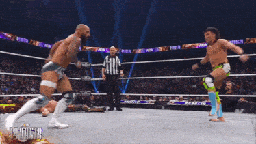 a wrestler is laying on the ground while another wrestler kicks him