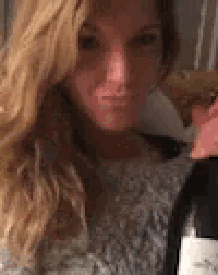 a woman is holding a bottle of wine and making a face .