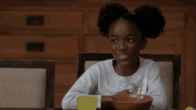 a young girl is sitting at a table with a bowl of food