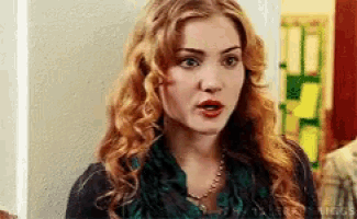 a woman with long red hair is wearing a green scarf and a black shirt .