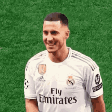 a soccer player wearing a white fly emirates jersey is smiling on a field .