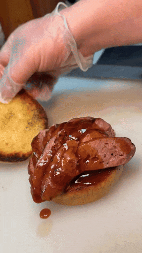 a person wearing clear plastic gloves is putting sauce on a sandwich