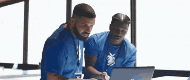 two men are looking at a laptop together .