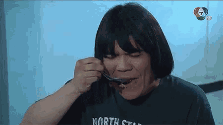 a man wearing a green north star shirt is eating something with a spoon .