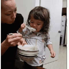 a little girl is eating noodles from a bowl