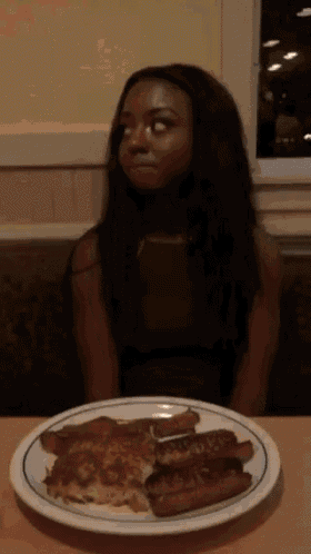 a woman sitting at a table looking at a plate of food