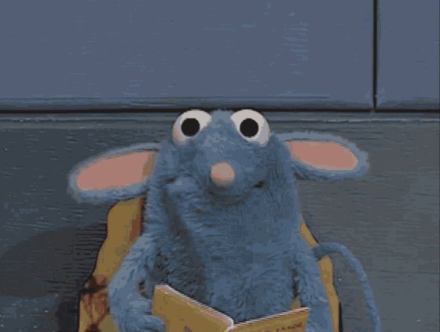 a stuffed mouse is reading a book while sitting in a chair