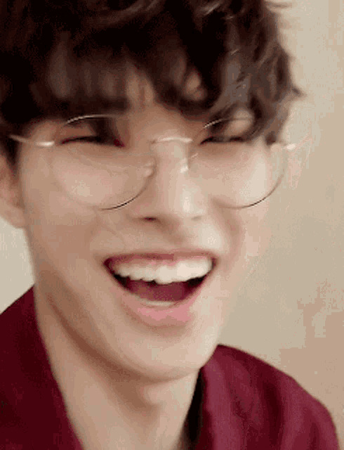 a young man wearing glasses is smiling with his mouth open .