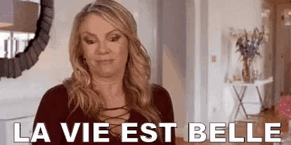 a woman is standing in front of a mirror in a living room and says `` la vie est belle '' .