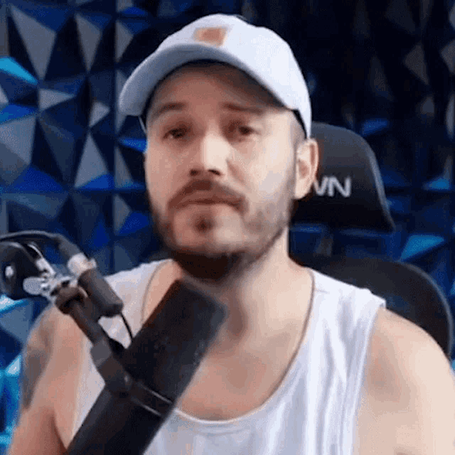 a man with a beard is sitting in front of a microphone wearing a hat and a tank top .