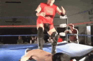 a wrestler in a red shirt is jumping over another wrestler in a ring .