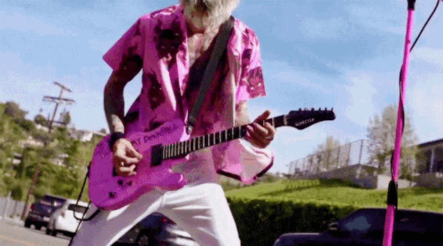 a man in a pink shirt is playing a pink electric guitar .