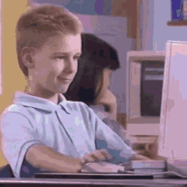a young boy is sitting at a desk in front of a computer and smiling .