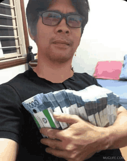 a man wearing glasses is holding a stack of 1000 bills in his hands