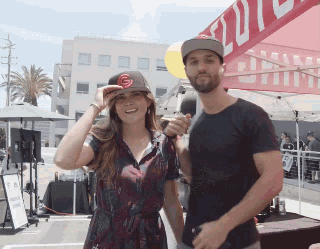 a man holding a microphone stands next to a woman wearing a hat with a g on it