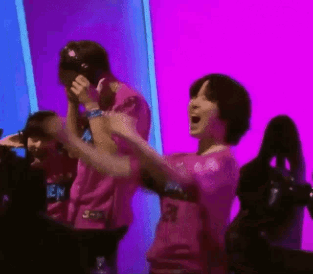 a group of people in pink shirts are dancing in front of a purple wall .