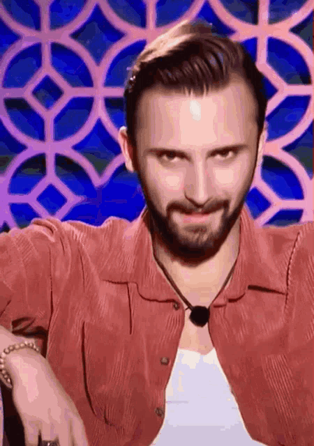 a man with a beard wearing a red shirt and a white tank top is making a funny face .