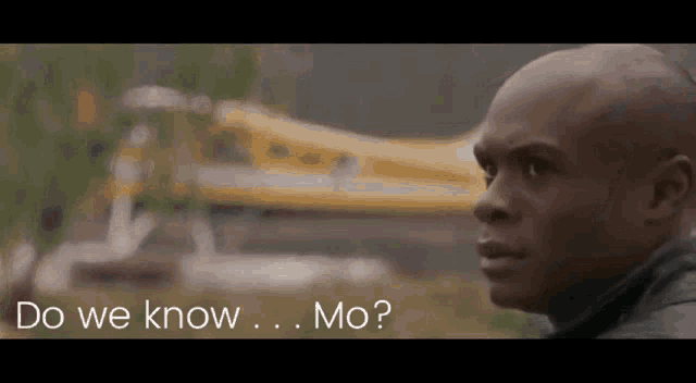 a bald man is standing in front of a yellow plane and asking do we know mo