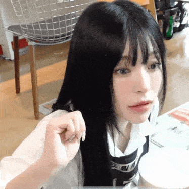 a girl with long black hair is sitting at a table with a chair in the background