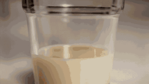 a glass of milk is being poured into a cup on a table .