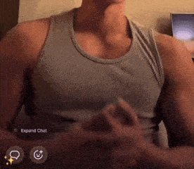 a man in a grey tank top is sitting in front of a computer screen that says expand chat on it