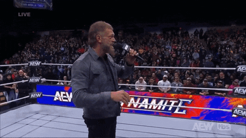 a wrestler is speaking into a microphone in front of a aew banner