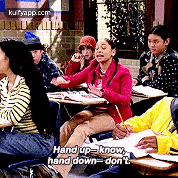 a group of people are sitting at desks in a classroom and one of them is talking on the phone .