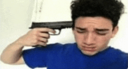 a man in a blue shirt is pointing a gun at his head .