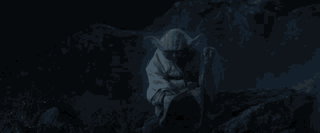 a statue of yoda sits on a rock in a dark cave
