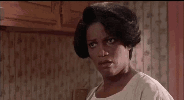 a woman is making a funny face in a kitchen while wearing a white shirt .