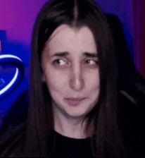 a woman with long dark hair is making a funny face in front of a purple background .