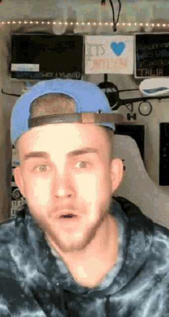 a man wearing a blue hat and a tie dye sweatshirt looks surprised