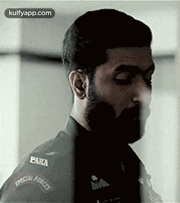 a man with a beard is wearing a special forces uniform and looking at the camera .