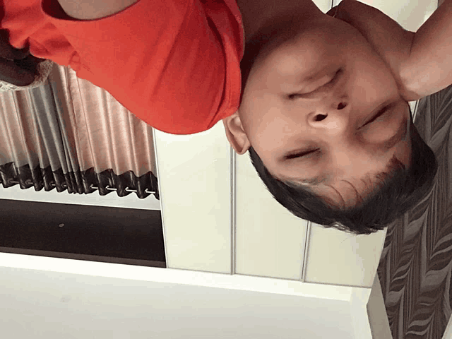 a person laying upside down with their eyes closed and a red shirt on