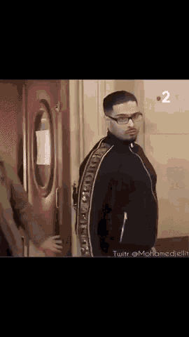 a man wearing glasses and a black jacket is standing in front of a door .