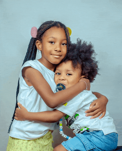 a little girl hugging a little boy with a pacifier in his mouth