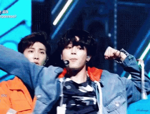 a man in a denim jacket is flexing his muscles on stage .