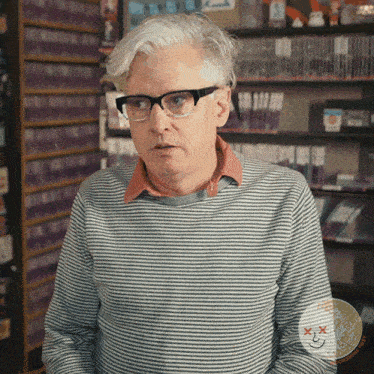 a man wearing glasses and a striped sweater is standing in front of a shelf full of books