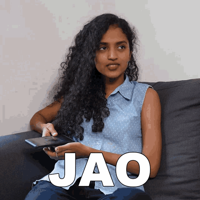 a woman is sitting on a couch holding a cell phone and the word jao is visible