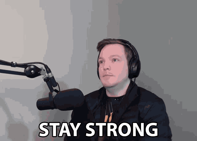 a man wearing headphones stands in front of a microphone with the words stay strong above him