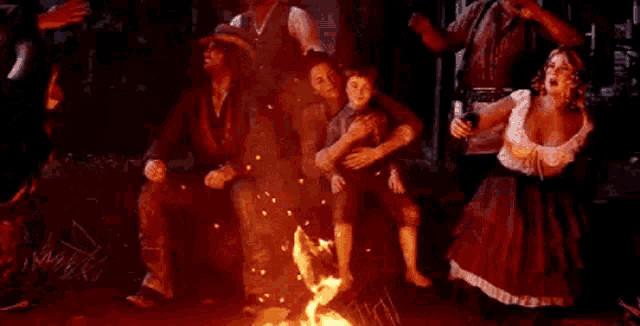 a group of people are standing around a campfire .