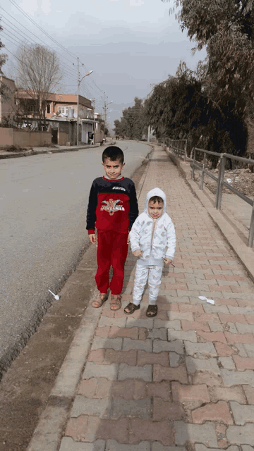two children walking down a sidewalk one of whom is wearing a shirt that says spiderman on it