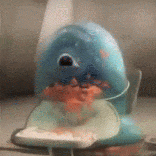 a toy shark is sitting on a table with a piece of food in its mouth .
