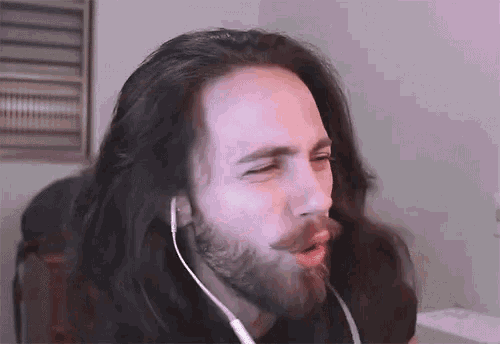 a man with long hair and a beard is wearing headphones and making a funny face