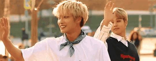 two young men are standing next to each other and waving their hands .